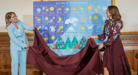 H.M. Dronningen og årets Julemærkekunstner Emilie Melgaard Jacobsen fjerner det røde klæde og afslører årets Julemærke 2025